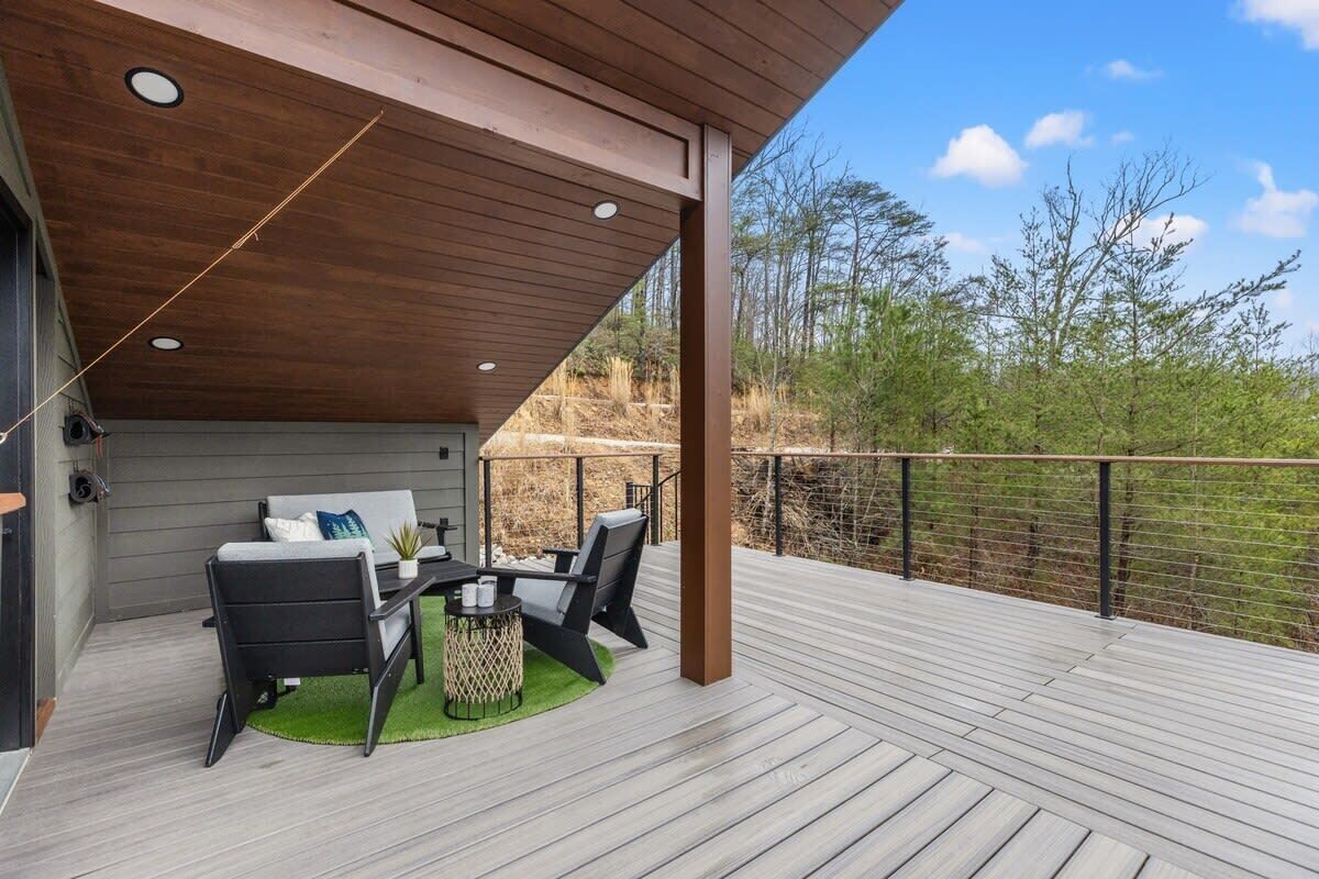 A covered outdoor deck with a dining area, including a table and chairs, and a view of the surrounding landscape.