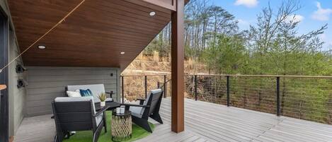 A covered outdoor deck with a dining area, including a table and chairs, and a view of the surrounding landscape.