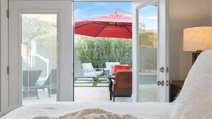 A hotel room with a bed, a notebook, and a pen on it. There is a sliding glass door leading to an outdoor patio with a red umbrella, a table, and chairs. - 3BD - Heated Pool - Pet friendly - N. Scottsdale (Cave Creek)