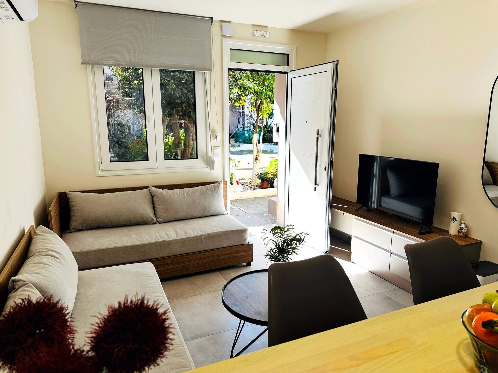 Una sala de estar moderna con sofá, televisión, mesa de comedor y vistas al exterior.
