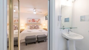 A hotel room with a bed, bedside lamps, a ceiling fan, a glass shower enclosure, and a white sink. - The Landmark unit 405 Resort style, spectacular water views, lift, linen, pool, games room, port-a-cot and highchair. (Nelson Bay)