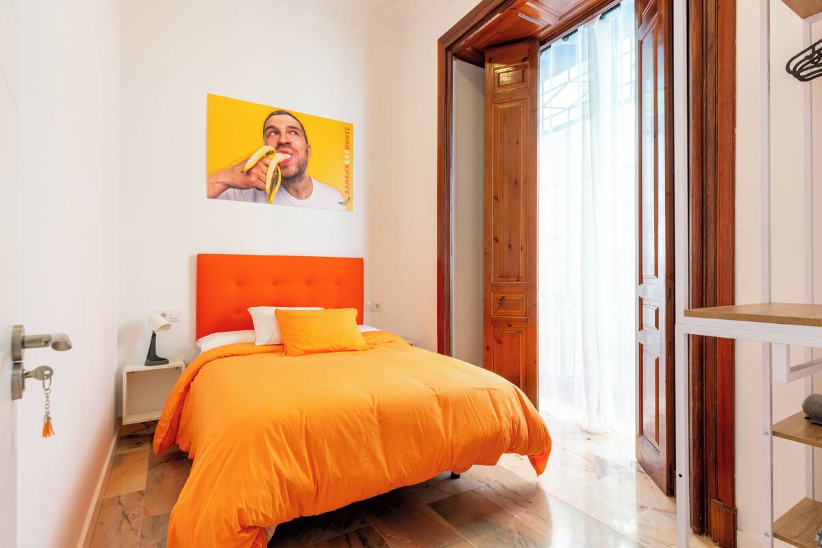 A bedroom with a large bed, a wooden door, and a bright orange wall.