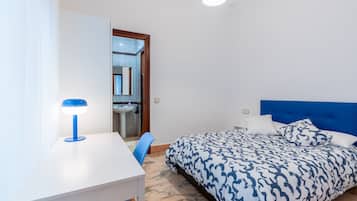 A bedroom with a bed, a desk, a chair, and a bathroom visible through an open door.
