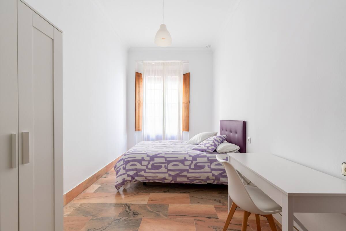 A bedroom with a bed, a desk, and a chair.