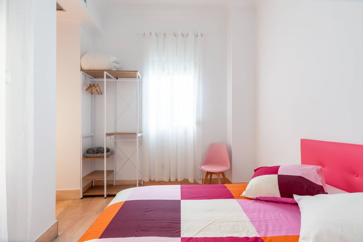A bedroom with a bed, a chair, a wardrobe, and a window with curtains.