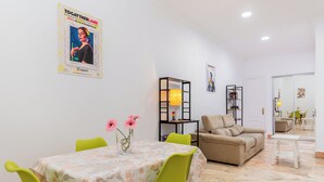 Uma sala de estar com uma mesa de jantar, cadeiras verdes, um sofá bege e um abajur.
