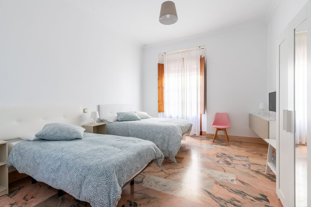 A modern hotel room with two beds, a desk, a chair, and a TV.
