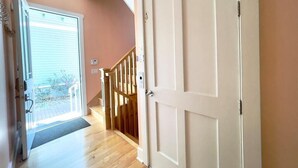 A hallway with a wooden staircase, a white door, and a view of the outside.