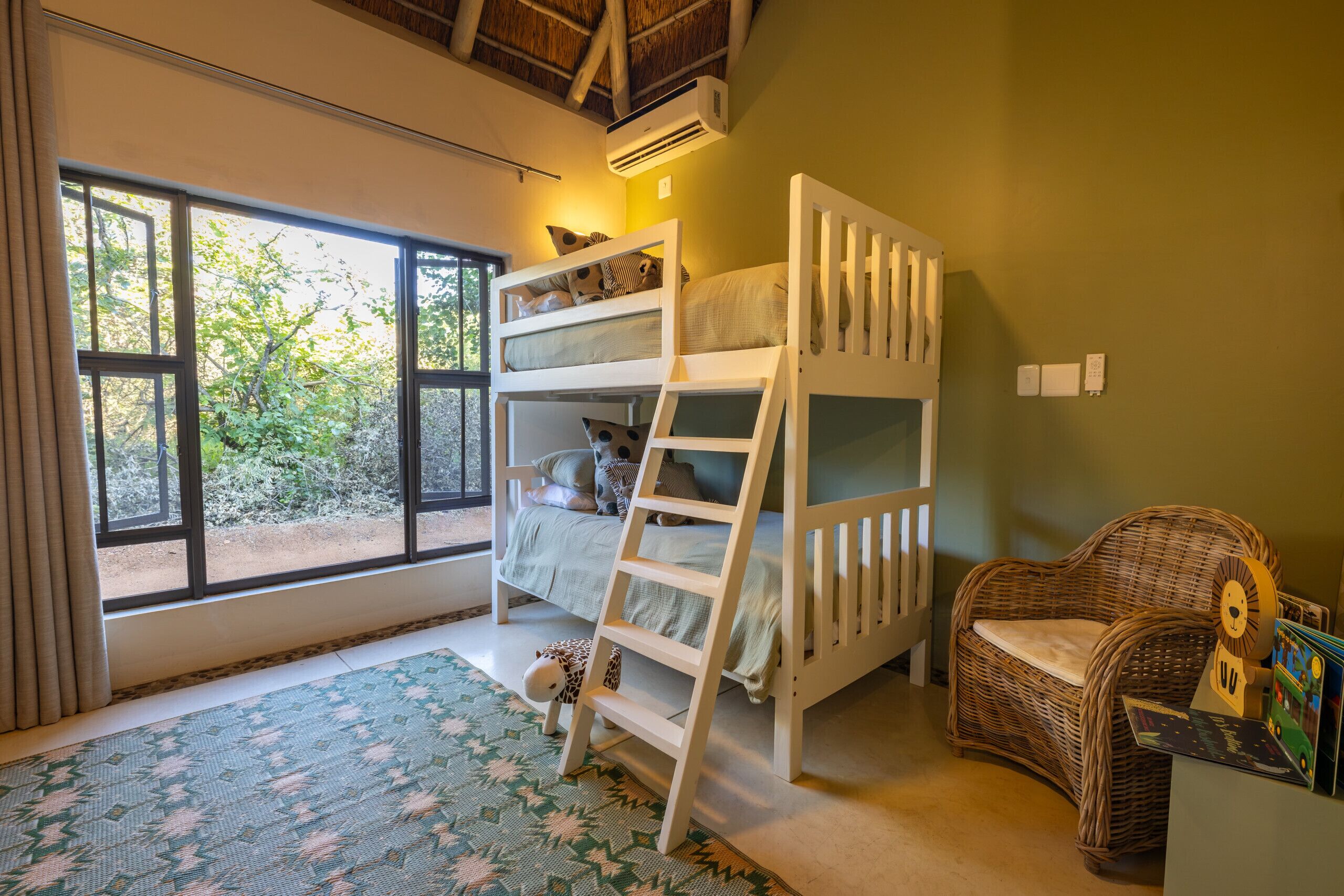 Ein Kinderstockbett mit einer Leiter, ein Korbstuhl und ein Fenster mit Blick auf Bäume.