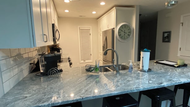 A kitchen with a marble countertop, stainless steel sink, and black bar stools. - Kelly's Cozy Golf Getaway/ Enclosed Patio/ Lakeside/Woodlake's Maples Golf Course on Site/Minutes from Fort Bragg/40 Plus Golf Courses Nearby/Sleeps 8 (Vass)