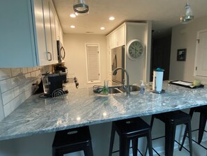 A kitchen with a marble countertop, stainless steel sink, and black bar stools.