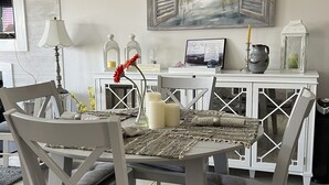 A dining area with a table set for four, surrounded by chairs. A painting of a beach scene hangs on the wall above the table. - Kelly's Cozy Golf Getaway/ Enclosed Patio/ Lakeside/Woodlake's Maples Golf Course on Site/Minutes from Fort Bragg/40 Plus Golf Courses Nearby/Sleeps 8 (Vass)