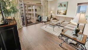 A spacious living room with a large sliding glass door leading to a balcony, a sofa set, a coffee table, and a lamp. - 9th Floor Tranquility: Spacious One-Bedroom Condo (North Myrtle Beach)