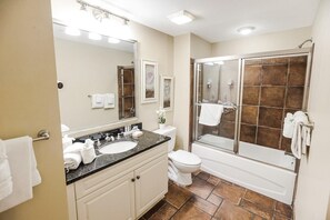 Bathroom features a granite countertop sink, a white toilet, and a glass-enclosed shower area with a bathtub.