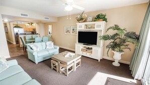 A living room with a sofa, coffee table, and TV stand. There is a kitchen in the background. - Luxurious Oceanfront 2 Bdrm Condo Stunning Views (North Myrtle Beach)