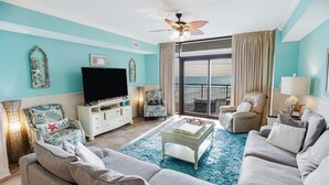 A living room with a sofa, armchairs, a coffee table, a TV, and a balcony with a view.