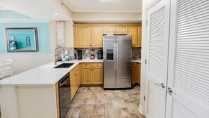 A compact kitchen with wooden cabinets, a stainless steel refrigerator, and a white countertop.