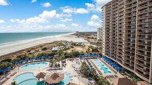 Un hôtel doté de plusieurs piscines, offrant une vue sur la plage et comprenant un grand bâtiment avec des balcons.