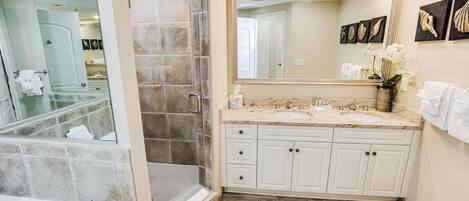 A bathroom with a bathtub, a shower, a sink with a large mirror, and a toilet.