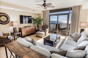 A spacious living room with a large sofa, a coffee table, and a TV. There's a balcony with a view of the ocean. - Experience Paradise: 3 Bedroom Beachfront Condo (North Myrtle Beach)