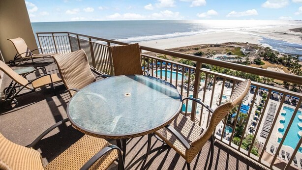 A balcony with wicker furniture, a glass table, and a view of the beach and pool area. - Relax in Style: Oceanfront 3 Bedroom Condo (North Myrtle Beach)