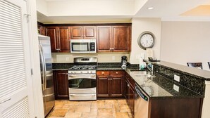 A modern kitchen with dark wooden cabinets, stainless steel appliances, and a granite countertop. - Coastal Comfort Redefined: 3 Bedroom Condo (North Myrtle Beach)