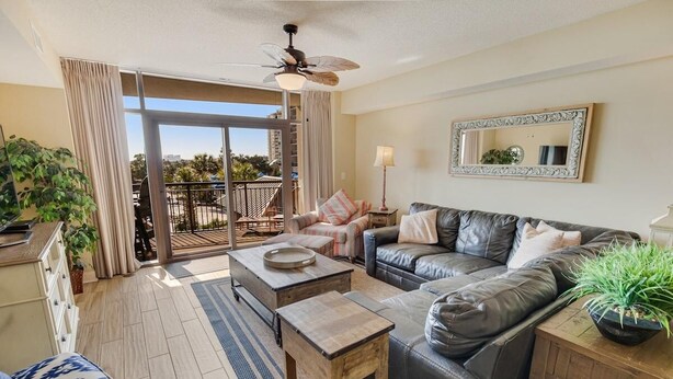A spacious living room with a sliding glass door to a balcony, a ceiling fan, a large mirror, and a potted plant. - Seaside Perfection 3 Bdrm Oceanfront w/ Whirlpool (North Myrtle Beach)