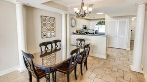 A dining area with a round table and chairs, a chandelier, and a kitchen in the background.