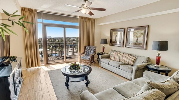 A spacious living room with a large sofa, a coffee table, and a chair. There is a balcony with a view of the landscape.