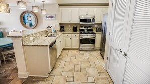 Une cuisine avec des meubles blancs, un plan de travail en granit, des appareils électroménagers en acier inoxydable et un sol carrelé disposé en motif chevron.
