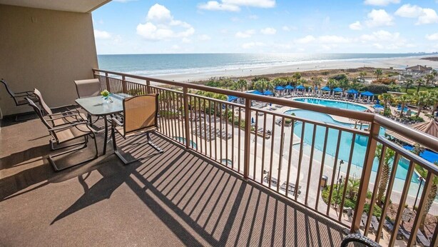 Un balcon avec vue sur la plage et une zone aménagée autour de la piscine.