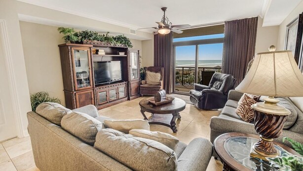 Un salón con sofá, sillones, televisión y un balcón con vistas.