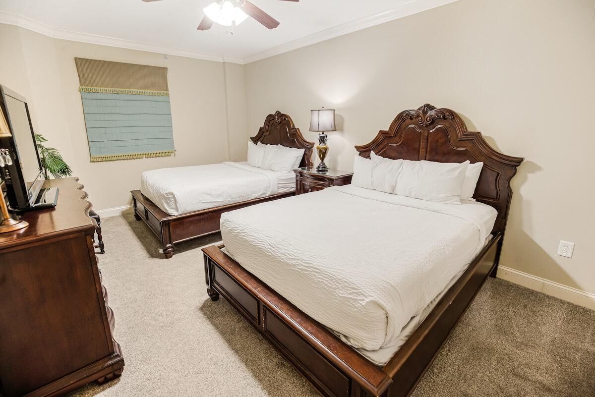 Ein Schlafzimmer mit zwei Einzelbetten, einer Holzkommode, einem Nachttisch mit Lampe und einem Deckenventilator.