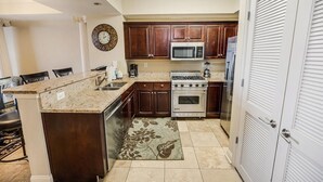 Una cocina con alacenas de madera oscura, un microondas blanco, una estufa y un refrigerador.