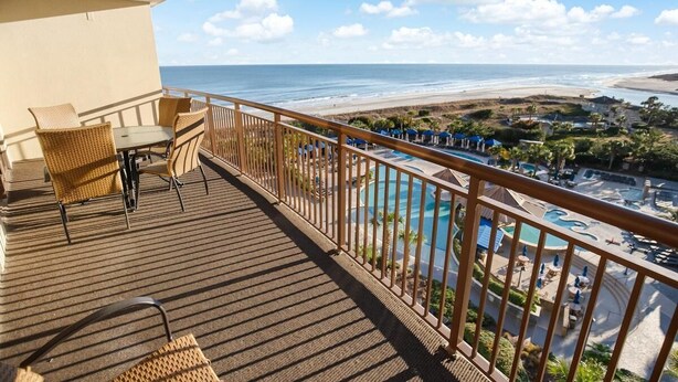 Un balcón con muebles de mimbre, piscina y vista a la playa y al océano.