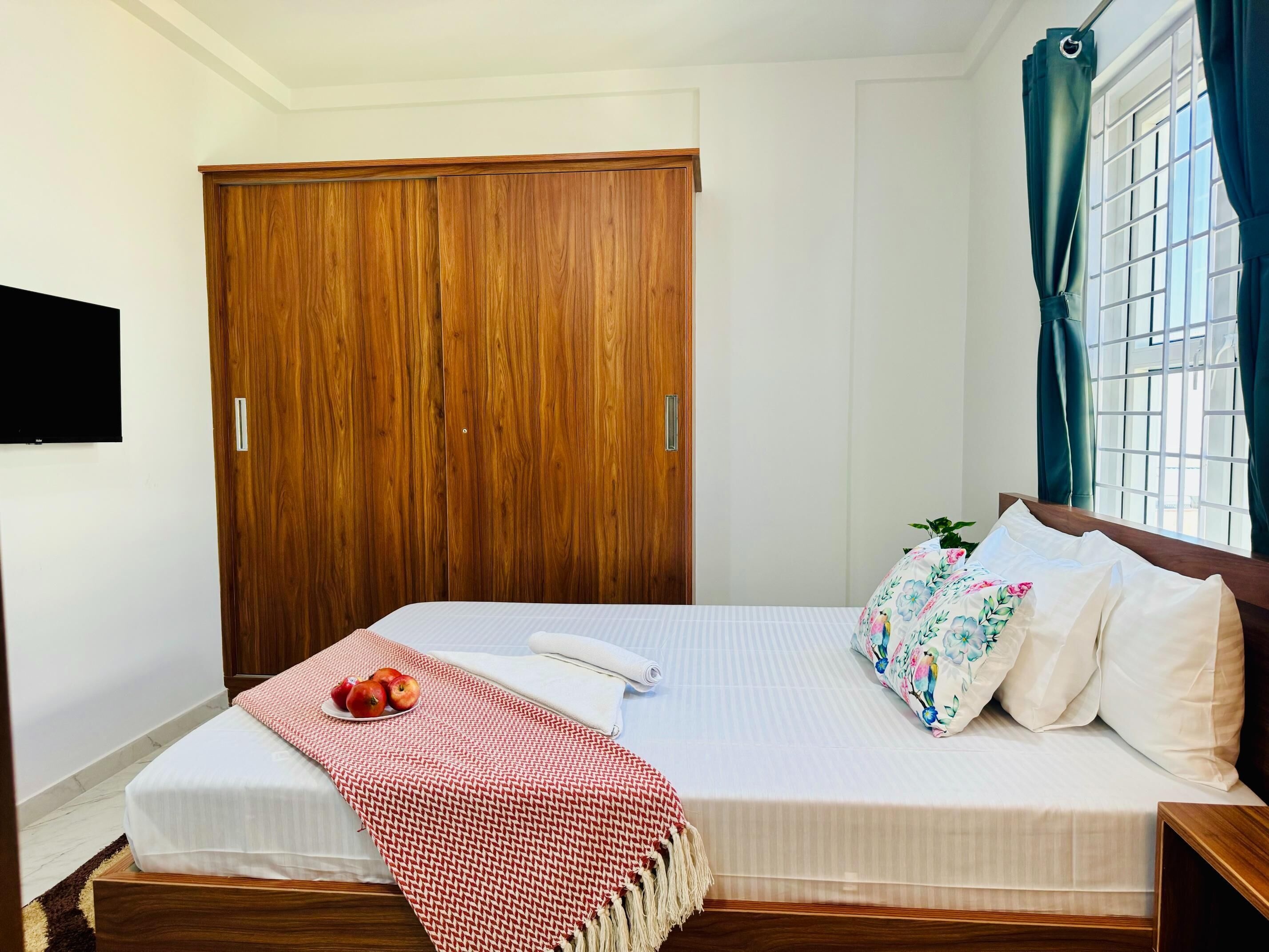 Un dormitorio con un armario de madera, una cama con ropa de cama floral, una mesita de noche y una ventana con cortinas.