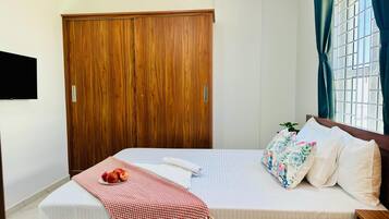Un dormitorio con un armario de madera, una cama con ropa de cama floral, una mesita de noche y una ventana con cortinas.