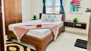 Un dormitorio ordenado con una cama de madera, una ventana con cortinas, una mesita de noche con una planta y una obra de arte colgada en la pared.