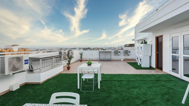 Una terraza en la azotea con césped artificial, una mesa con sillas y vistas a la ciudad.