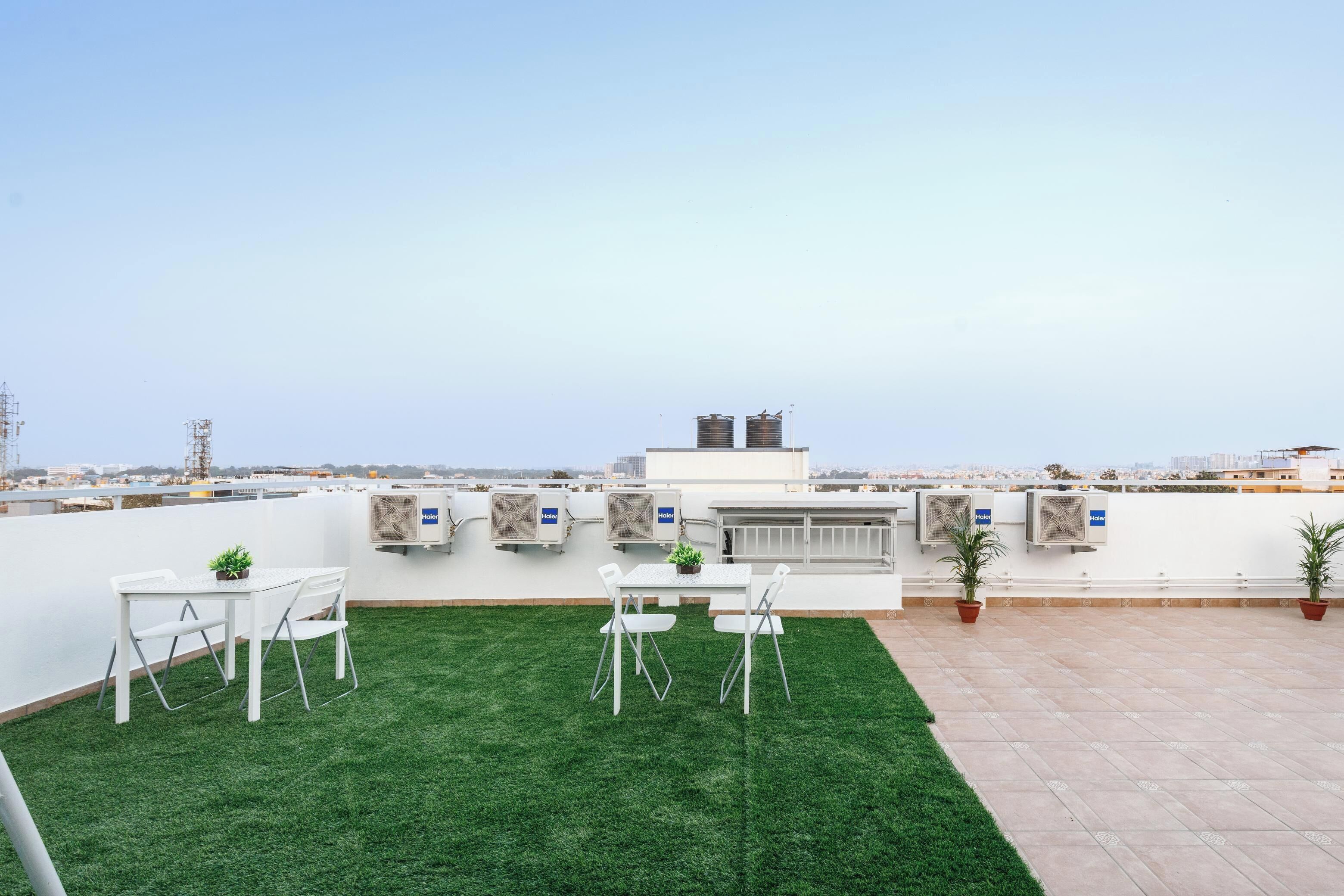 Een dakterras met kunstgras, witte tafels en stoelen, en plantenpotten.