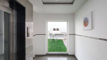 Un pasillo con puerta de cristal que da a un balcón con césped verde y vista a edificios.