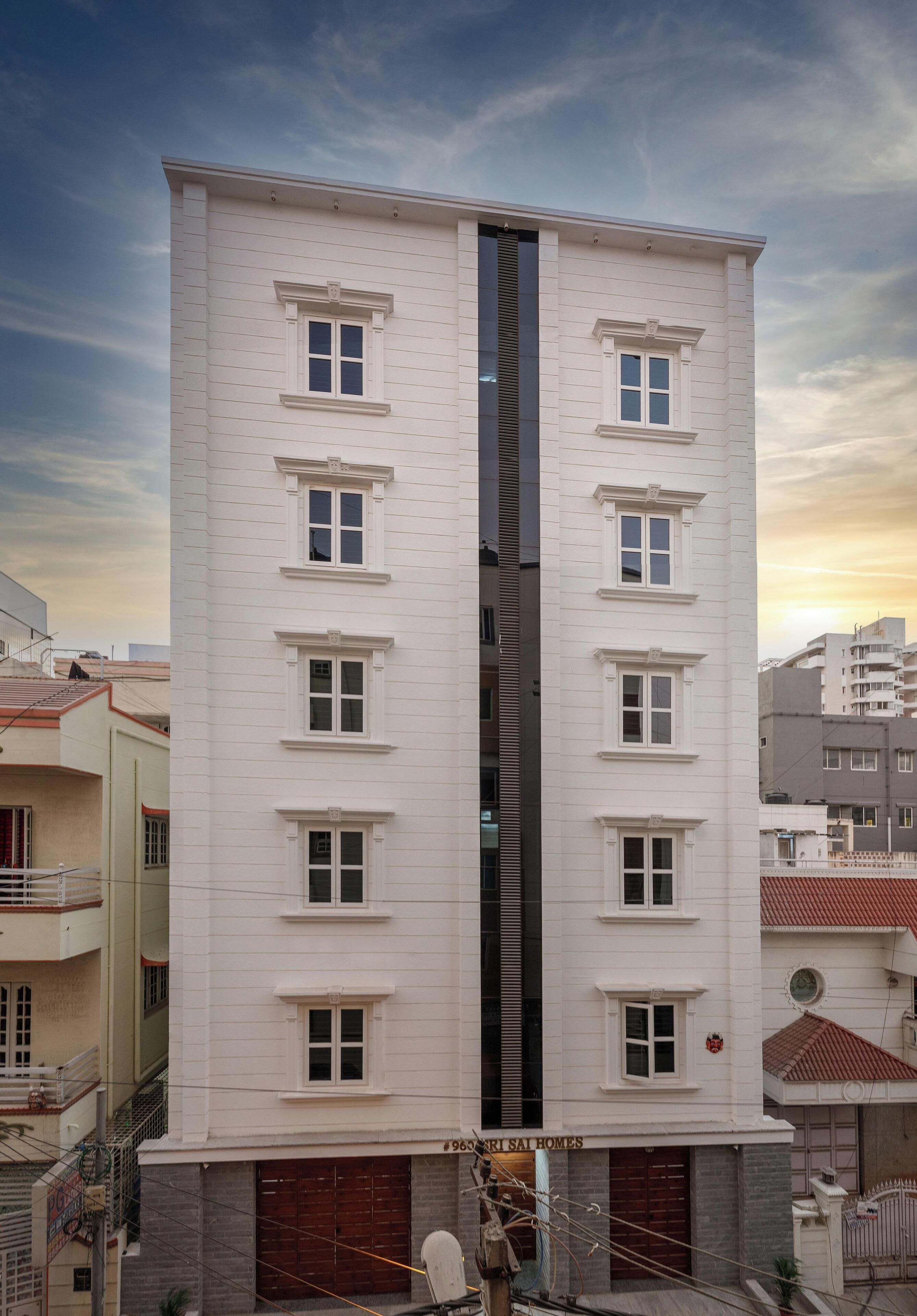 Un edificio de varios pisos con un elemento vertical negro central, numerosas ventanas y un garaje en la base.