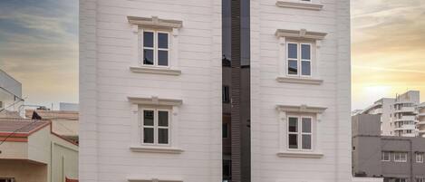 Un edificio de varios pisos con un elemento vertical negro central, numerosas ventanas y un garaje en la base.