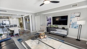 A modern living room with a dining area, a kitchen in the background, and a large flat-screen TV mounted on the wall. - 3 Bedroom Condo with King and Queen Sized Beds (North Myrtle Beach)