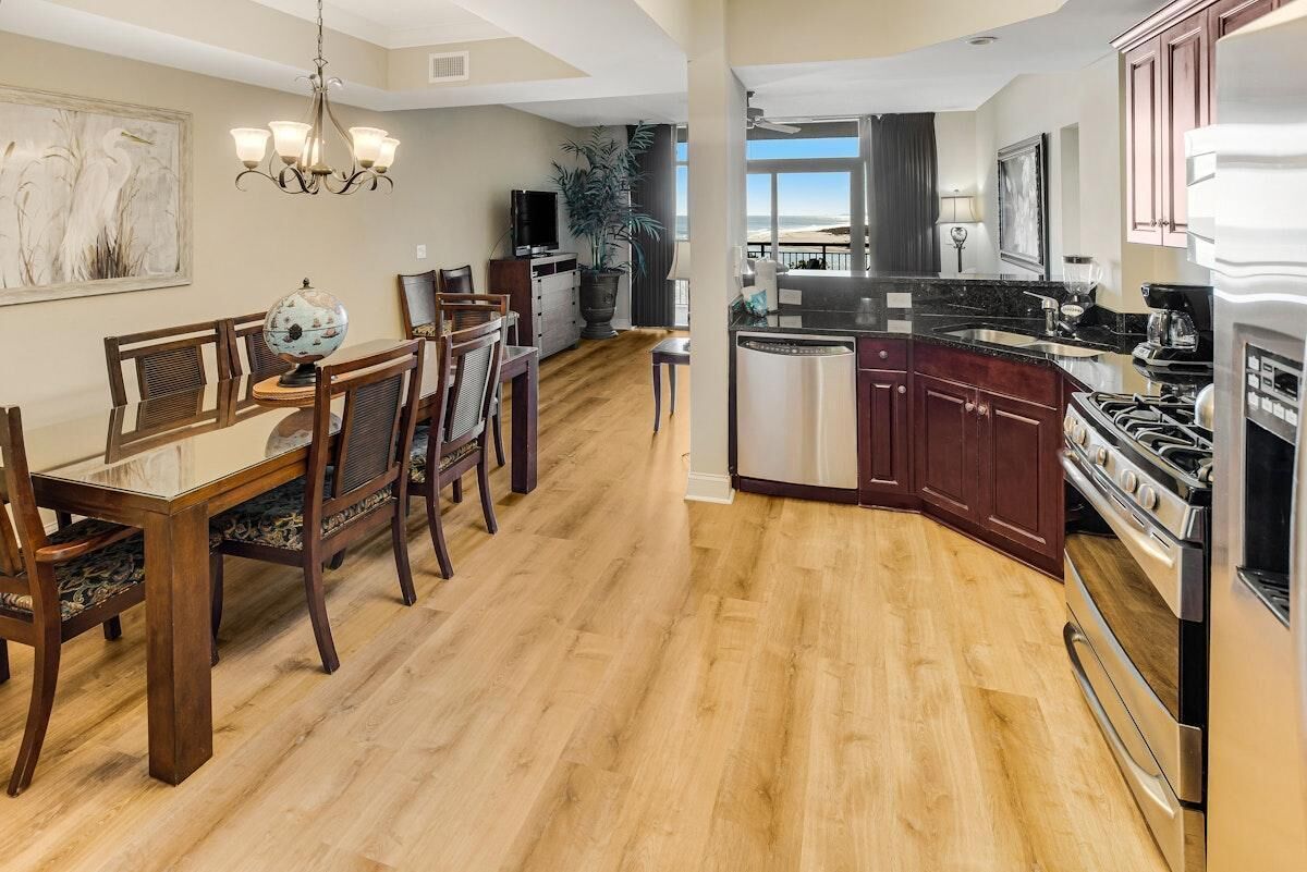 A modern kitchen with dark wooden cabinets, stainless steel appliances, and a dining area with a wooden table and chairs.
