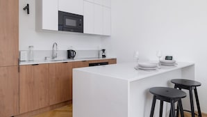 Una cocina moderna con armarios blancos, un microondas negro, una cafetera y una pequeña isla con taburetes.