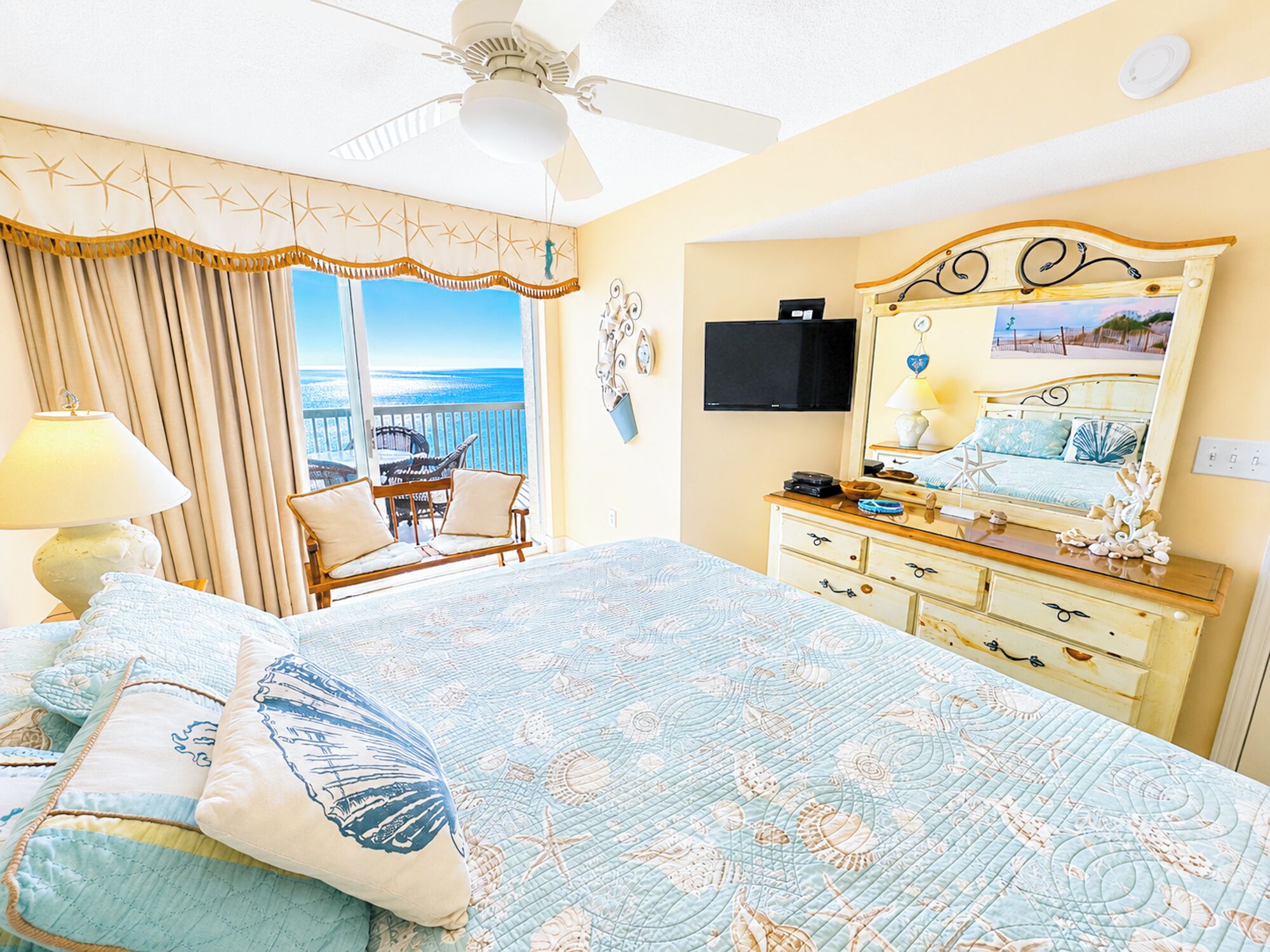 Un dormitorio con cama, cómoda, televisor, ventilador de techo, ventana con vistas y una silla.