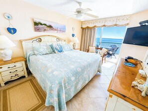 Un dormitorio con cama, escritorio, silla, televisor y balcón con vistas.