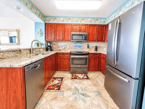 A kitchen with wooden cabinets, stainless steel appliances, a dishwasher, and a tiled floor. - Ashworth 1608 (North Myrtle Beach)