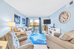 A living room with a sofa, armchairs, a coffee table, a TV, and a large wall clock.